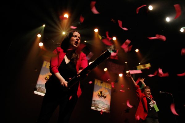 A woman with brown hair shoots out confetti from on stage